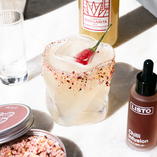 Margarita with chili seasoning, Listo bottle, and chili infusion bottle on a white surface